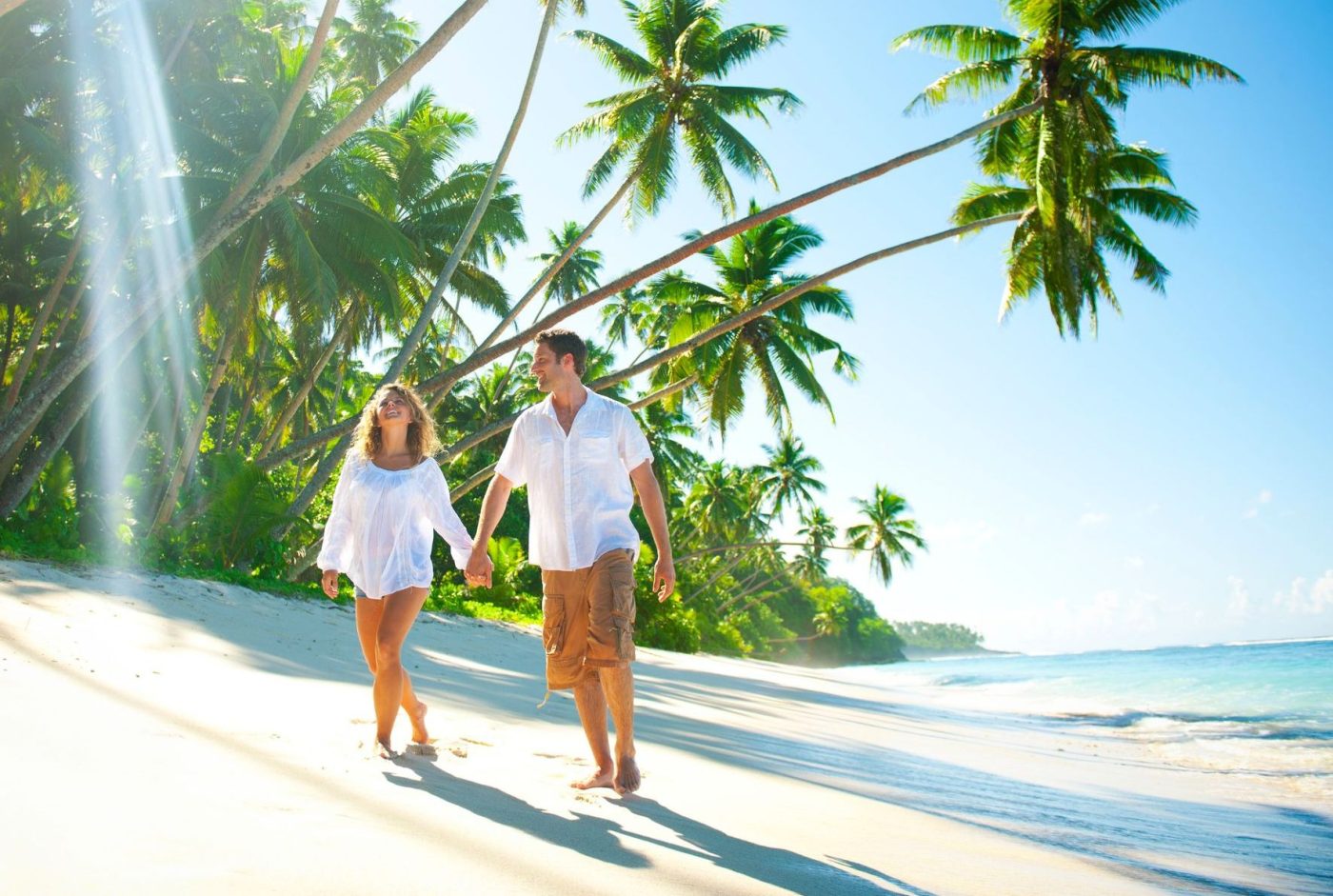 Young Couple relaxing on an idyllic tropical beach after taking out diverticulitis travel insurance.
